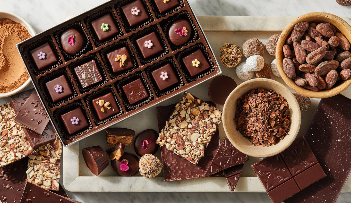 A box of chocolate bonbons, chocolate bars and chocolate truffles are spread out on a marble table.