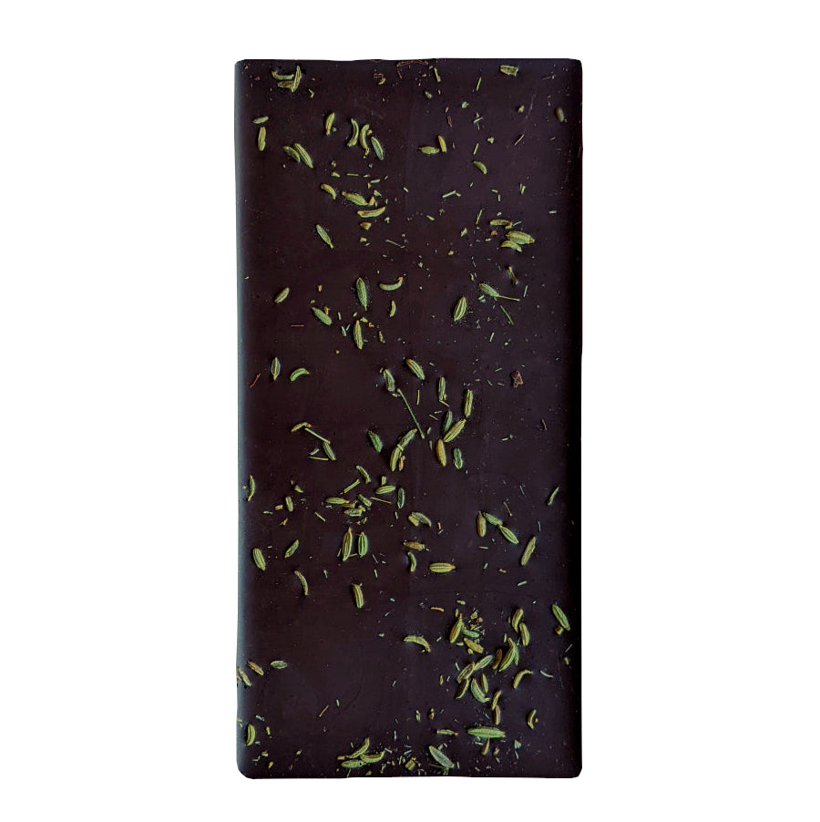 The back of a dark chocolate bar sprinkled with light green toasted fennel seeds on a white background.