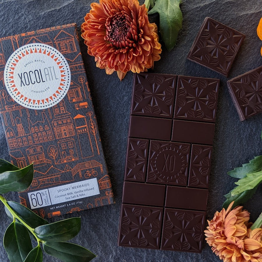 Xocolatl Chocolate bar wrapped in a Halloween-themed black and orange wrapper with unwrapped chocolate bar and orange marigold flowers.