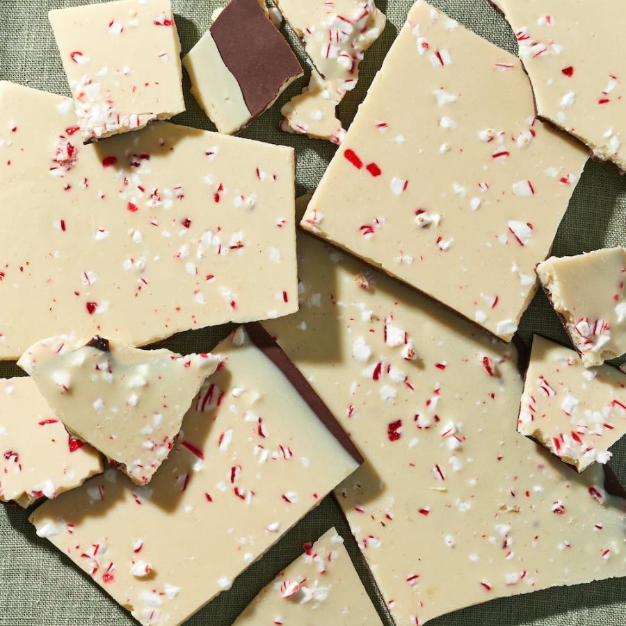 A close up of several pieces of peppermint bark made of layers of white & dark chocolate & topped with crushed red & white peppermint candy.