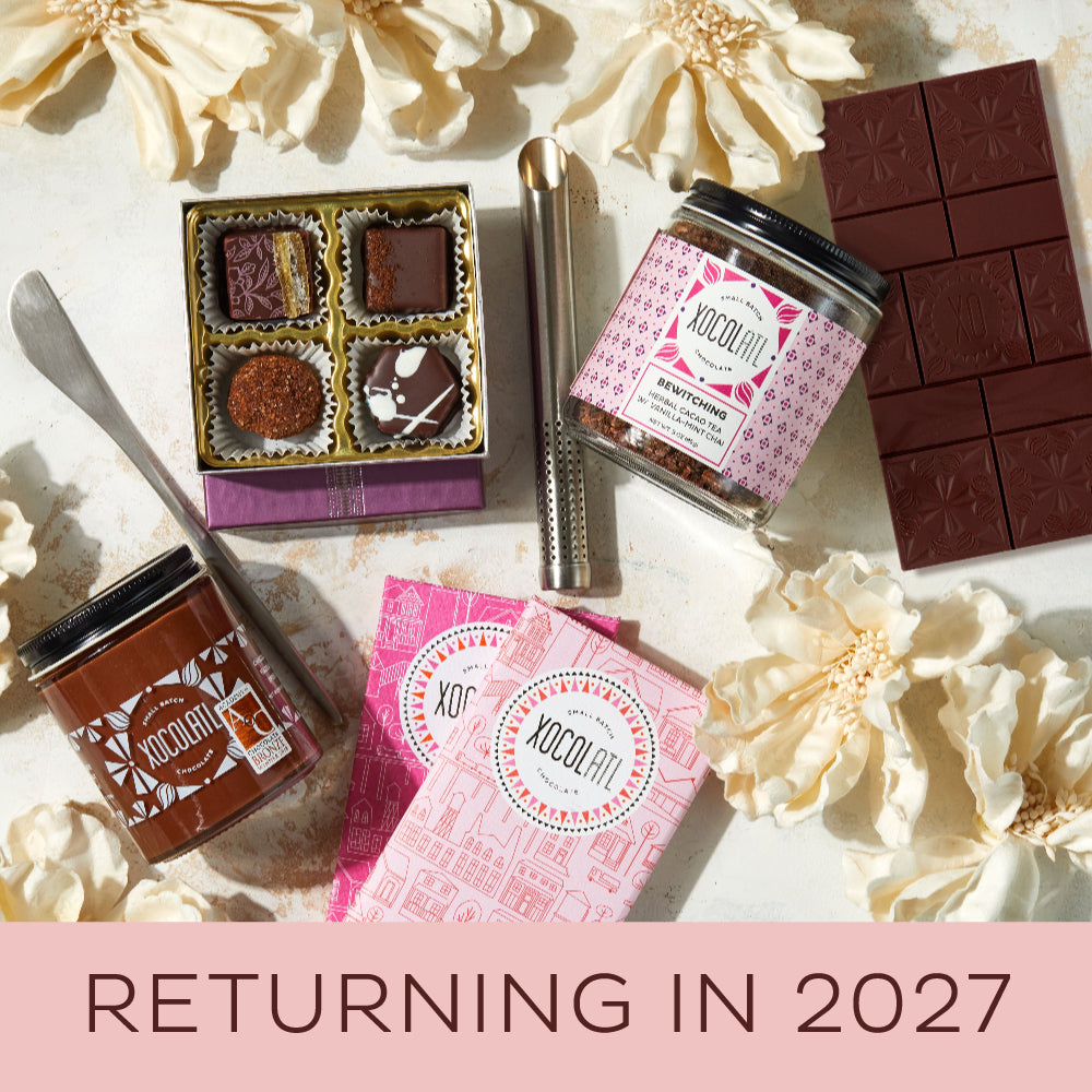 Assorted chocolate products including bars, truffles, and containers on a light surface with flowers.