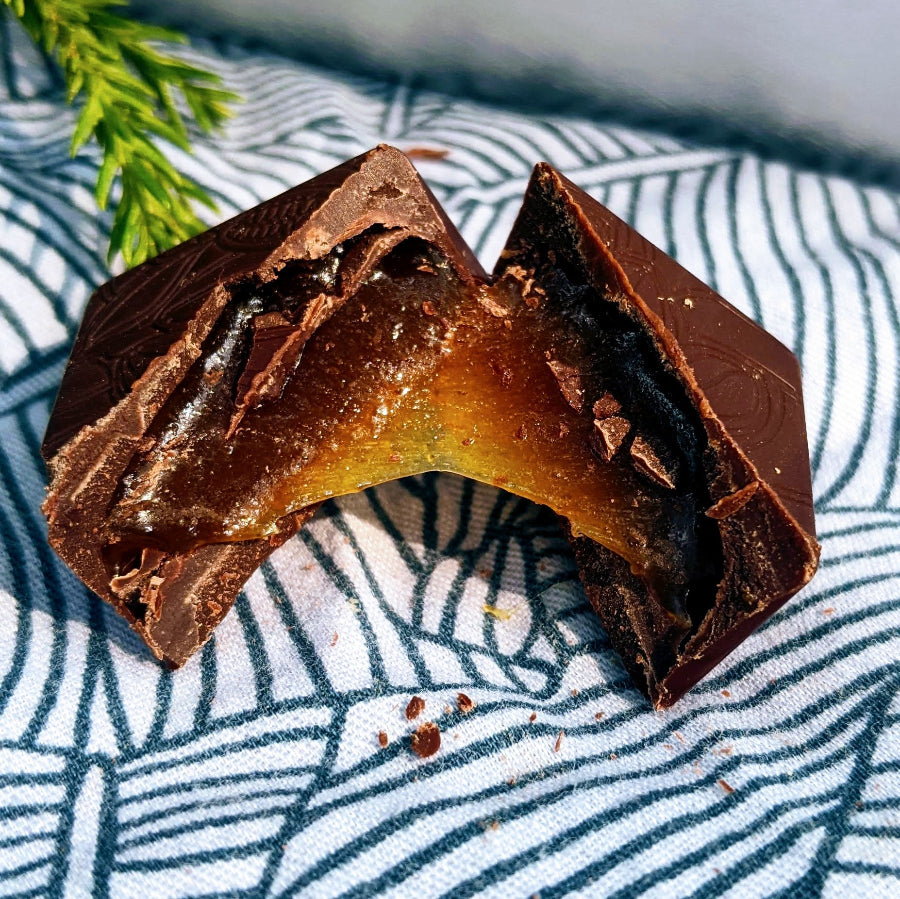A chocolate bonbon is cut in half showing an amber colored caramel filling inside.