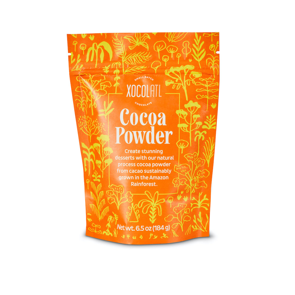 The front of an orange and yellow Xocolatl Chocolate Cocoa Powder paper pouch printed with a pattern of whimsical jungle foliage.