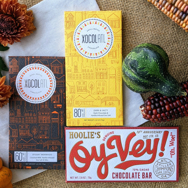 3 Xocolatl Chocolate bars called Spooky Mermaids, Dark & Salty, and Oy Vey on a textured background with fall gourds and flowers