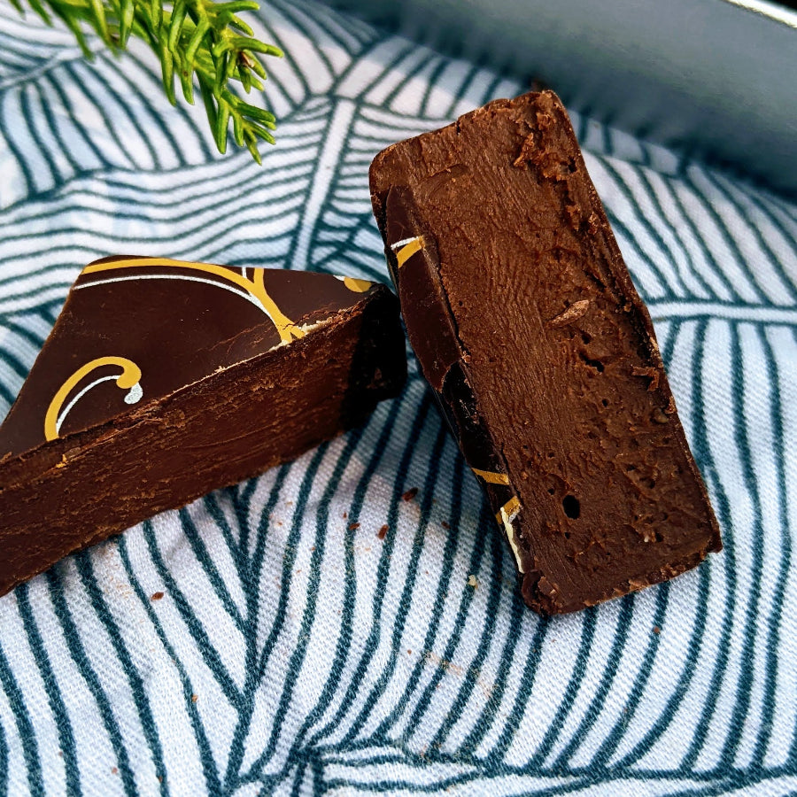 A chocolate bonbon with a decorative gold pattern is cut in half showing a creamy chocolate ganache filling inside.