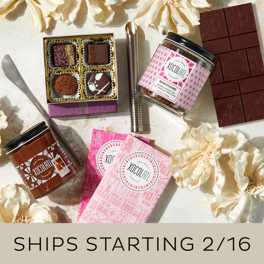 Assorted chocolate products including bars, truffles, and containers on a light surface with flowers.