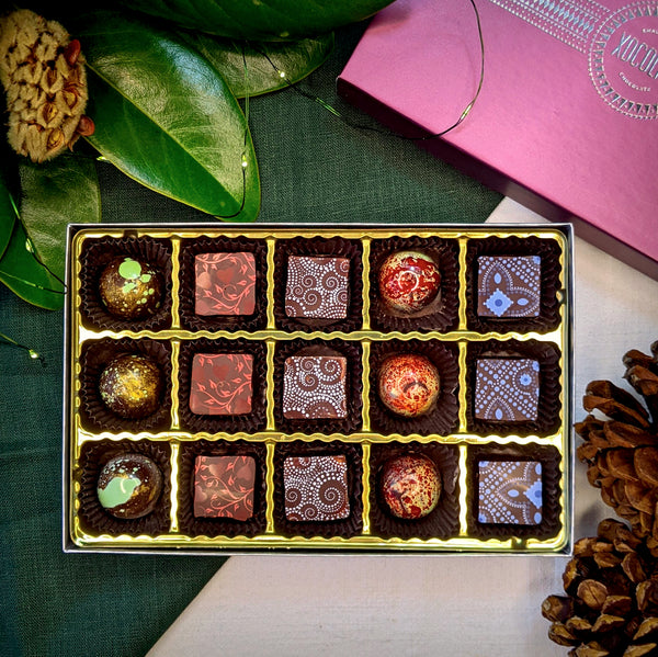 Box of chocolates with decorative patterns on a marble surface, accompanied by a purple box.