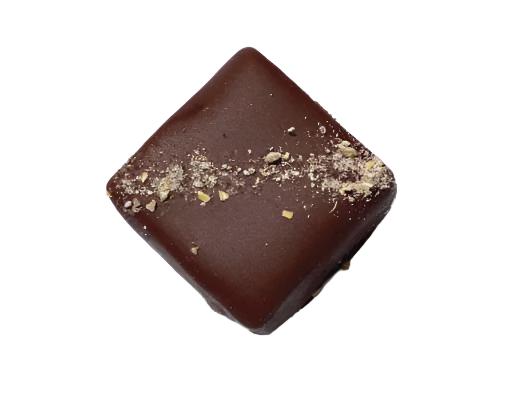 A square chocolate bonbon with a diagonal sprinkle of sea salt decorating the top on a white background.