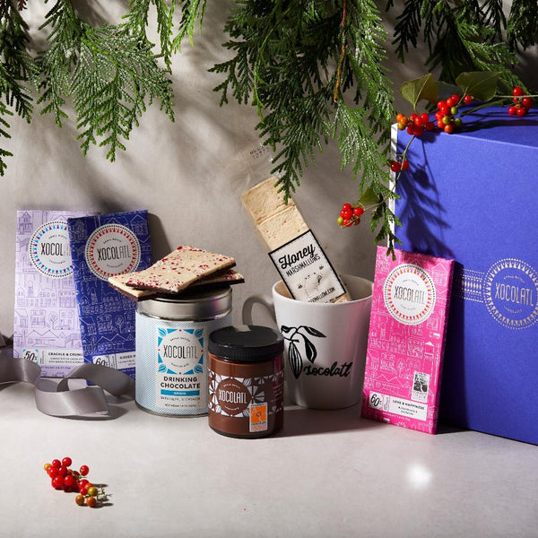 A gift box containing various chocolate products and a mug, neatly arranged with a decorative ribbon and pine branch decorations in the background.