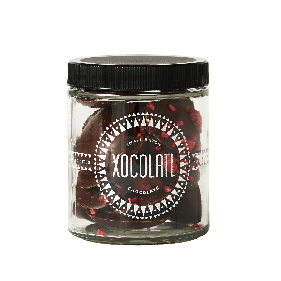 A glass jar with the Xocolatl Chocolate logo in white is filled with heart-shaped dark chocolate pieces, all on a white background.